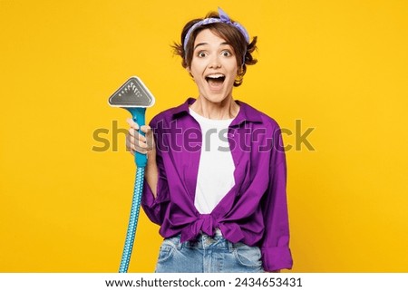 Young shocked surprised woman wears purple shirt casual clothes do housework tidy up hold in hand steamer look camera isolated on plain yellow color background studio portrait. Housekeeping concept