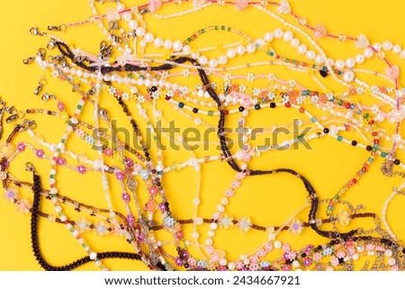 Multicolored chains of beads, pearls and natural stones scattered on a yellow background.