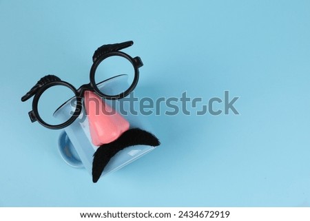 Man's face made of cup, fake mustache, nose and glasses on light blue background, top view. Space for text