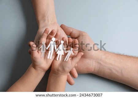 Parents and child holding paper family figures on gray background, top view Royalty-Free Stock Photo #2434673007