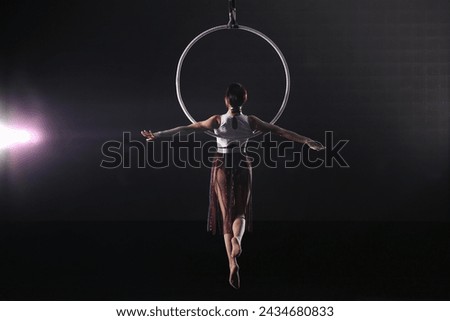 Young woman performing acrobatic element on aerial ring against dark background Royalty-Free Stock Photo #2434680833