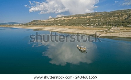Clouds reflected on the lake and a boat travelling on the lake. Forest and mountain in the background. Lake Burdur, Turkey.