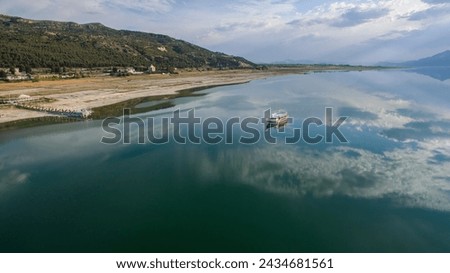 Clouds reflected on the lake and a boat travelling on the lake. Forest and mountain in the background. Lake Burdur, Turkey.