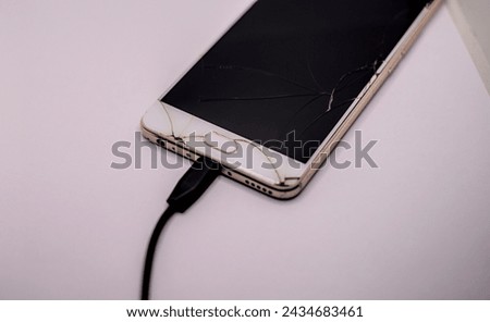 Smartphone with cracked screen and cable on grey background