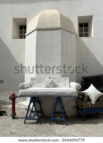 Arrangement with white sofa on blue posts,  white pillow, black cat and red fire pump Essaouira Morocco