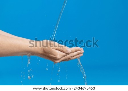 Woman hands catching water on blue background.