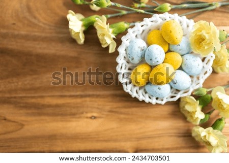 Yellow flowers and pastel yellow and blue colored eggs in a white small wicker basket on a background of brown wood. Layout. Mockups. Pastel Springs background. Easter background. Easter eggs close up