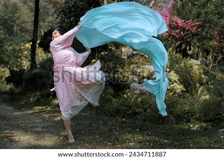 Pretty Asian girl in a beautiful elegant ancient Chinese costume traditional dress dancing with a flowing shawl made of thin long fabric pastel color waving in the wind at a green natural garden. 