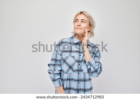 Young woman in plaid shirt looking thoughtful, isolated on light background.