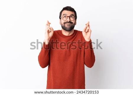 Caucasian handsome man with beard over isolated white background with fingers crossing and wishing the best