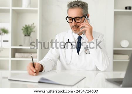 The mature doctor is pictured in a moment of ease, smiling while speaking on the phone, a stethoscope draped around his neck, portraying a friendly and reassuring medical consultation, taking notes