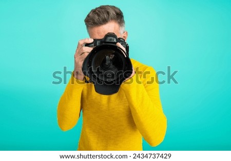Photographing with camera lens. Man photographer isolated on blue. Photographer hold photo camera. Professional photography. Shooting session. Photoshoot. Man taking photo picture. Selective focus
