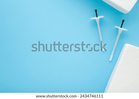 White plastic insulation anchor dowels and styrofoam panels on pastel blue table background. Closeup. Material for house thermal protection. Home facade repair work preparation. Empty place for text.