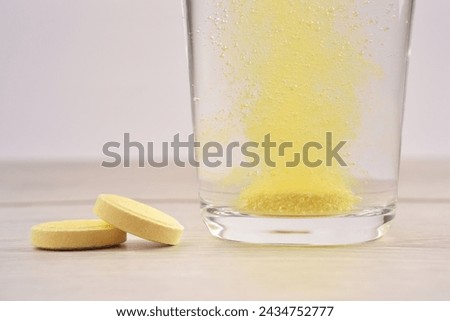 Close up of orange colour water soluble vitamin C dissolving in glass of water with bubbles photographed on wooden surface