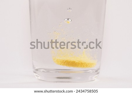 Close up of orange colour water soluble vitamin C dissolving in glass of water with bubbles photographed on white or light background