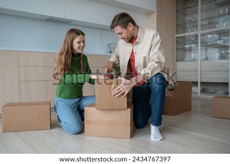 Joyful boyfriend and girlfriend excitedly preparing to move new place. Couple carefully packs things into cardboard boxes, trying not forget anything. Man and woman looking forward to new home moving. Royalty-Free Stock Photo #2434767397