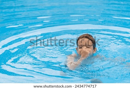 adorable little boy dipping in the blue pool, while holding his nose and making ripples in the water Royalty-Free Stock Photo #2434774717