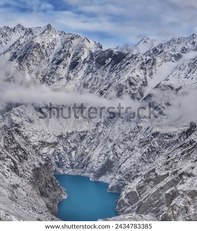 The beauty of the photo is captivating. The serene blue water of the lake reflects the clear sky above, creating a sense of tranquility. Snow-capped mountains stand tall in the background, their peaks