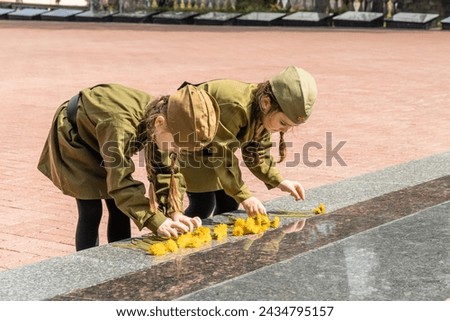 Patriotic education of youth. Little girls in an old Soviet military uniform laying flowers at the eternal flame near the monument to fallen soldiers in world War II. Victory Day on May 9. Copy space