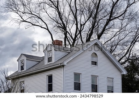 Classic American suburban style family home with a beautiful large tree bare branches in the background on a cloudy winter day in Brighton, MA, USA