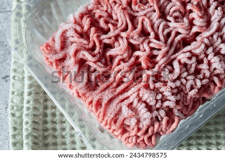 Frozen beef steak mince in a plastic container defrosting. On a green tea towel. Royalty-Free Stock Photo #2434798575