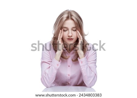 A young tired girl sits at a table and puts her hands on her head. Cute blonde girl in a pink shirt. Work, study and stress. Isolated on a white background.