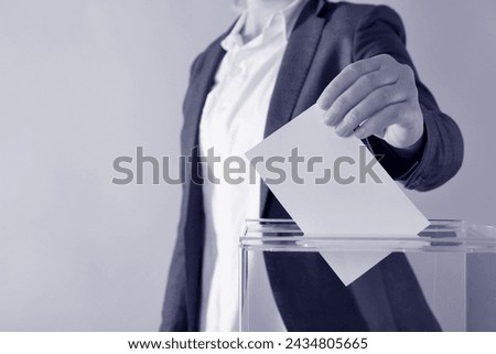Woman putting her vote into ballot box on background, closeup. Color toned Royalty-Free Stock Photo #2434805665