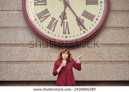 Watch the time concept. woman in dark red dress with cold tea next to huge watch over her head . Young brunette woman is looking at clock. Keep track of time. High quality photo