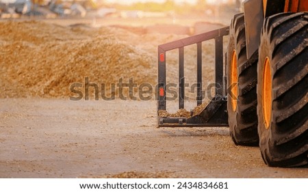 Tractor with pitchfork working with unloading silage at dairy farm, compacting fresh harvest chopped maize with heavy roller for silo, fermented feed for food of cow. Royalty-Free Stock Photo #2434834681