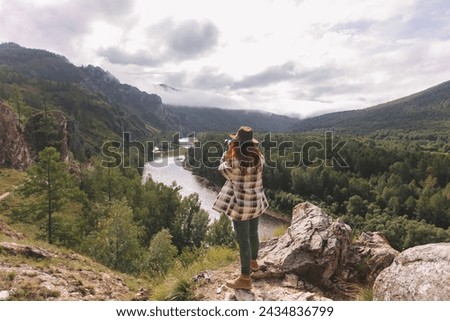 A young female tourist in a hat takes pictures of the mountains. Hiking on the Shaman's path, Khakassia, Russia