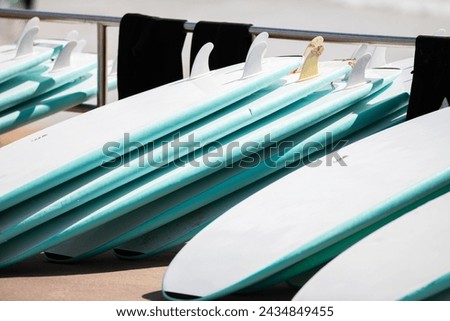 Stacked surfboards and cold ocean wetsuits hanging on the railings dry in the sun and await the next surf school students. High quality close-up stock photo