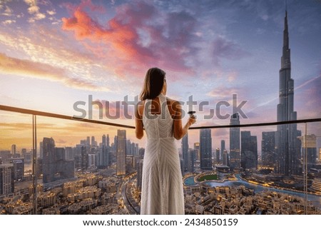 A elegant woman in a white evening dress enjoys the beautiful sunset view behind the modern skyline of Downtown Dubai, UAE