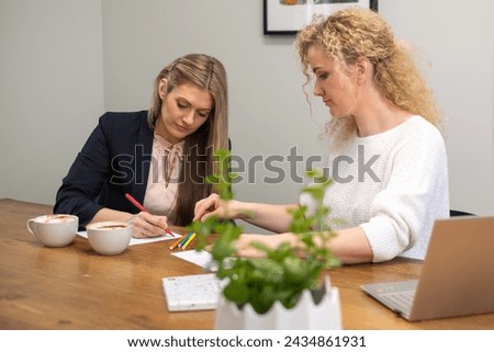 Two focused women work together at a table with coffee and laptops, symbolizing collaboration, planning, and teamwork in a professional workspace. High quality photo
