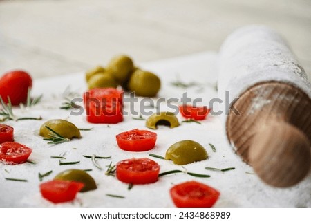 Preparing a focaccia with cherry tomatoes and olives and rosemary leaves.