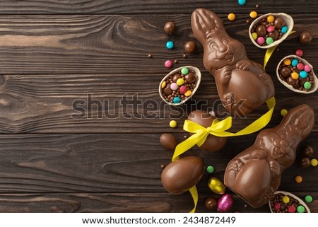 Festive Easter sweets display. Top view photo featuring chocolate eggs broken open with colorful candy inside, a chocolate bunnies, and ribbon on a wooden background, with space for wording or ads
