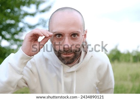pretty bearded young man 30 years old in glasses looks intently through lenses, concept human health, optimism in adulthood, regular eye checkups for maintaining visual health Royalty-Free Stock Photo #2434890121