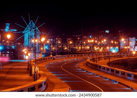 Long exposure photography of the winding road and the windmill on a splendid night in Nesebar, Bulgaria with hundreds of night lights.