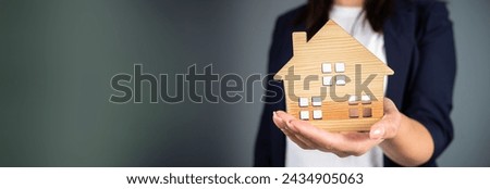 Woman holding a model of a house in her hand on a gray background
