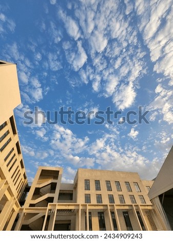 The picture shows a big building with a colorful sunset sky behind it. The sky has shades of blue, white, and a bit of orange, making it look really pretty.
