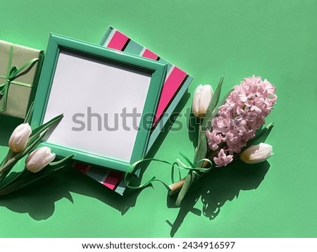 A picture frame is placed next to a fragrant bouquet of spring flowers, featuring white tulips and pink hyacinth in full bloom.
