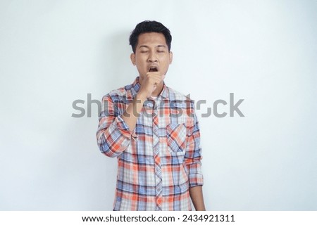 Portrait of exhausted and sleepy young handsome man yawning standing on white isolated background in studio. Bored male feels sleepy, yawns as feels tired, opens mouth widely, closed eyes.