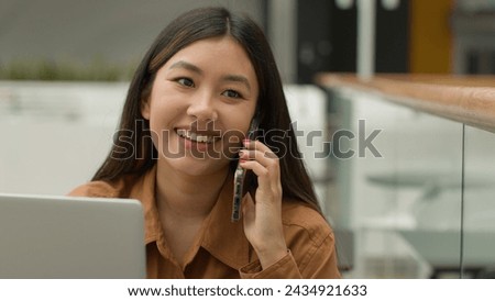 Smiling Asian woman businesswoman working online with laptop in office chinese japanese girl student freelancer talk mobile phone laughing excited female answer smartphone call carefree conversation Royalty-Free Stock Photo #2434921633