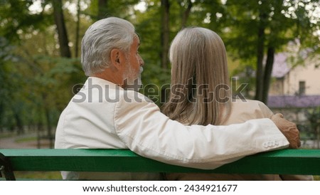 Back view cute positive 70s elderly couple retired happy family relaxing outdoors city nature park bench. Married spouse Caucasian man woman hugging enjoying healthy lifestyle talking together outside Royalty-Free Stock Photo #2434921677