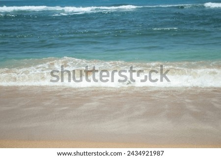 Soft waves of blue sea with foam on golden white sandy beach. Wave background