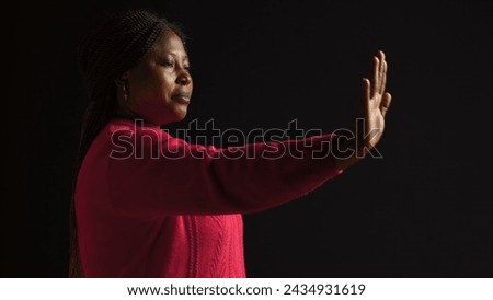 African american woman firmly signals stop using hand gesture in isolated black background. Female fashion model expresses disapproval rejecting and disagreeing in side-view portrait shot. Royalty-Free Stock Photo #2434931619