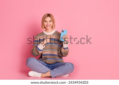 Full size photo of optimistic cheerful woman wear ornament pullover sit on floor directing at smartphone isolated on pink color background