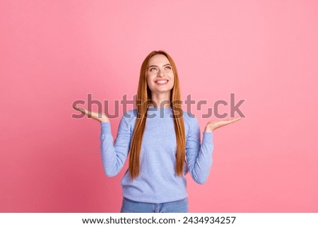 Photo of pleasant friendly woman dressed blue shirt palms presenting objects look up at empty space isolated on pink color background