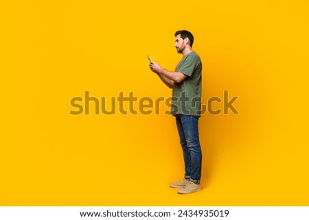 Full size photo of attractive young man hold device eshopping dressed stylish khaki clothes isolated on yellow color background