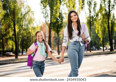 Photo of two adorable cheerful girls hold arms carry backpack walk cross road sunny weather street outside