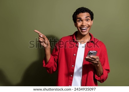 Photo of impressed funky man dressed red shirt typing apple iphone samsung device showing empty space isolated green color background